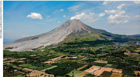 IMAGEM: ao fundo, fotografia de um vulcão soltando fumaça. no entorno, plantações e vegetação. FIM DA IMAGEM.