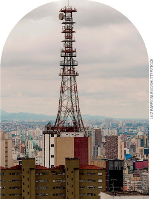 IMAGEM: uma antena de comunicação em cima de um prédio alto. ao redor, diversos prédios de apartamentos. FIM DA IMAGEM.