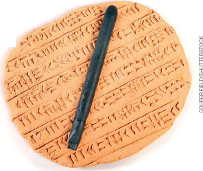 IMAGEM: fotografia de um tablete de barro contendo escrita cuneiforme. sobre o tablete, uma haste com extremidade em formato de cunha. FIM DA IMAGEM.
