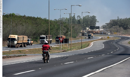 IMAGEM: uma rodovia onde estão passando uma moto e alguns caminhões. FIM DA IMAGEM.
