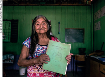 IMAGEM: idosa de etnia indígena segurando um livro nas mãos. FIM DA IMAGEM.