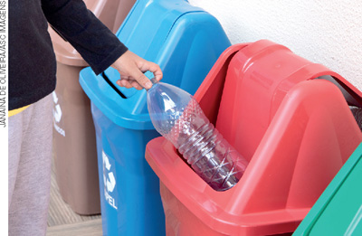 IMAGEM: pessoa descartando uma garrafa de plástico em uma lixeira para reciclagem. FIM DA IMAGEM.