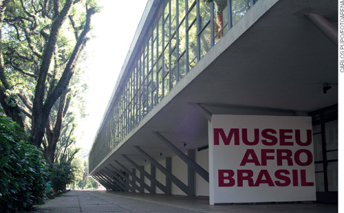 IMAGEM: fachada do museu afro brasil. edifício moderno, retângular de concreto e vidros. ao redor, muitas árvores. . FIM DA IMAGEM.