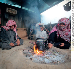 IMAGEM: um casal e um garotinho estão sentados ao redor de uma fogueira, onde eles parecem cozinhar algo. o homem e a mulher estão com lenços em suas cabeças e roupas típicas da palestina que cobrem o corpo inteiro. FIM DA IMAGEM.