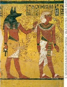 IMAGEM: um homem com cabeça de chacal é ilustrado próximo a outro homem com rosto humano, e roupas características de faraó. FIM DA IMAGEM.