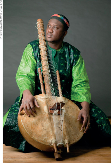 IMAGEM: homem segurando um instrumento de madeira e vestido com roupas da cultura africana. FIM DA IMAGEM.