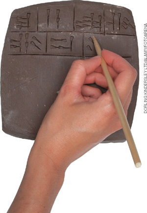 IMAGEM: pessoa escrevendo símbolos, com o auxílio de um instrumento de madeira, em um pedaço retangular de argila. FIM DA IMAGEM.