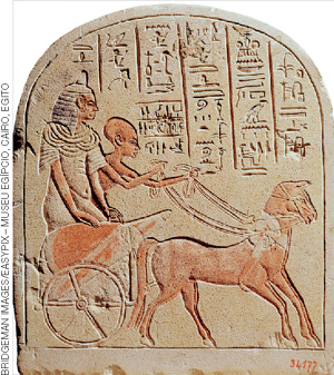 IMAGEM: placa de pedra com o desenho de um faraó e seu servo guiando um cavalo, os dois estão sobre uma carruagem egípcia. acima deles, há alguns escritos ordenados em colunas. FIM DA IMAGEM.