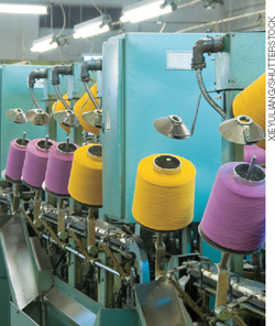 IMAGEM: máquinas com rolos de fios em uma indústria de tecido. FIM DA IMAGEM.