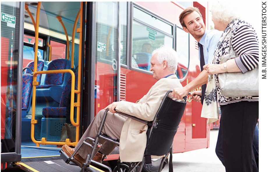 IMAGEM: dois idosos, com um deles sentados em uma cadeira de rodas, estão sendo auxiliados por um homem a subir num veículo de transporte público. FIM DA IMAGEM.