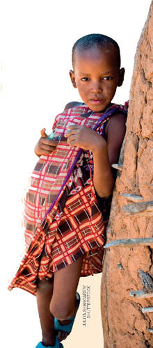 IMAGEM: uma menina encostada em uma parede de barro. ela usa um vestido quadriculado e sandálias. FIM DA IMAGEM.