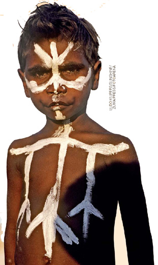 IMAGEM: um menino aborígene com o rosto e o corpo pintado com tinta branca. FIM DA IMAGEM.