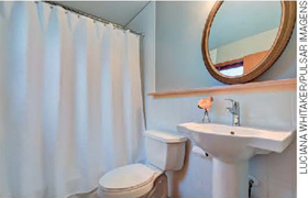 IMAGEM: um banheiro com uma pia, um espelho redondo, o vaso sanitário e uma cortina separando a área do chuveiro. FIM DA IMAGEM.