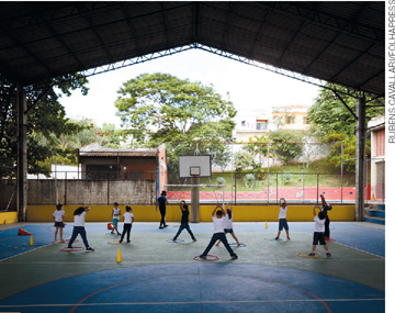 IMAGEM: crianças fazem atividades físicas em uma quadra escolar. FIM DA IMAGEM.