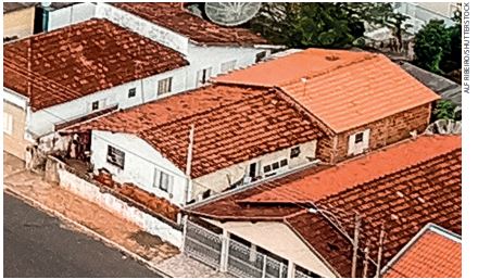 IMAGEM: a fotografia aproximada mostra a vista aérea de 3 casas feitas de concreto e tijolos, com telhas marrons e pinturas claras. a imagem está focada na casa do centro. FIM DA IMAGEM.