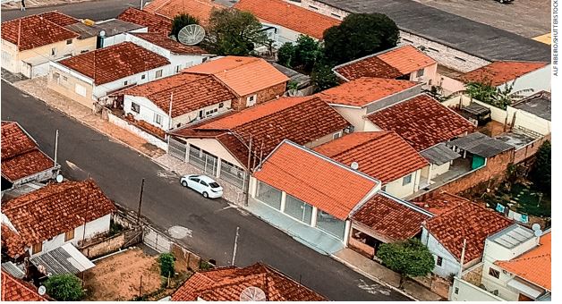 IMAGEM: vista aérea de várias casas divididas em quarteirões e com uma rua asfaltada no centro. FIM DA IMAGEM.