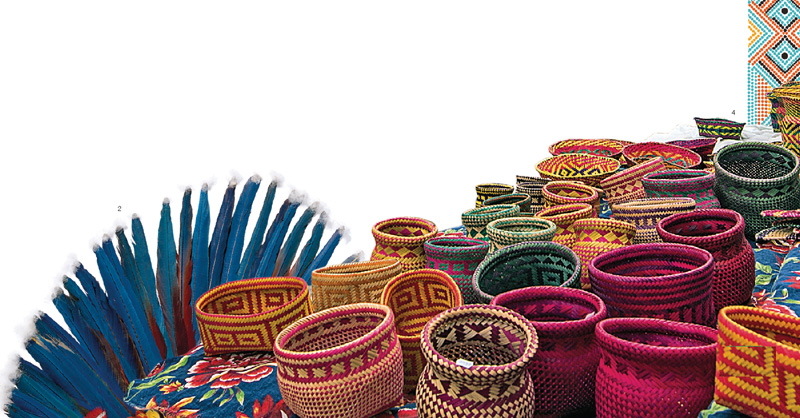 IMAGEM: Artesanatos da cultura indígena, potes trançados com palha, tecidos coloridos e penas. FIM DA IMAGEM.