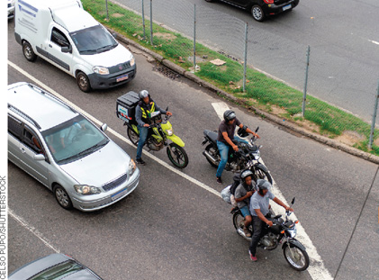 IMAGEM: carros e motos trafegam por uma rua movimentada de uma grande cidade. FIM DA IMAGEM.