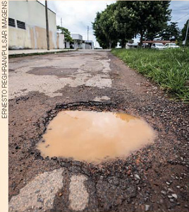 IMAGEM: buraco cheio de água enlameada no asfalto de uma rua. FIM DA IMAGEM.