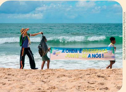 IMAGEM: pessoas carregando sacos de lixo na areia de uma praia. duas pessoas carregam uma faixa onde está escrito a onda é preservar, junte-se a nós!. FIM DA IMAGEM.