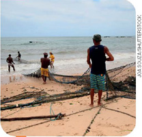 IMAGEM: homens entrando no mar com redes de pesca. FIM DA IMAGEM.