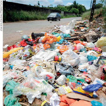 IMAGEM: grande quantidade de lixo descartado na beira de uma estrada. o lixo é formado por sacos plásticos, embalagens, caixas de papelão e restos de alimentos. FIM DA IMAGEM.