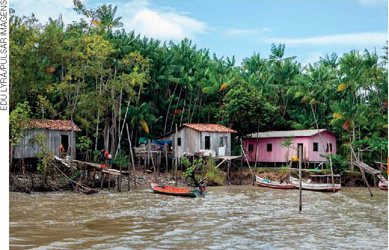 IMAGEM: casas sustentadas por vigas de madeira encontram-se na beira de um rio, onde alguns pequenos barcos estão ancorados. FIM DA IMAGEM.