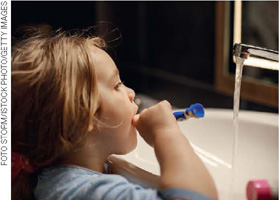 IMAGEM: menina escovando os dentes e deixando a torneira da pia aberta. FIM DA IMAGEM.