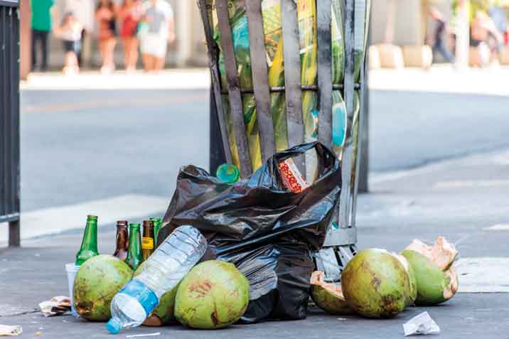 IMAGEM: saco de lixo aberto espalhando garrafas e cocos na calçada. FIM DA IMAGEM.