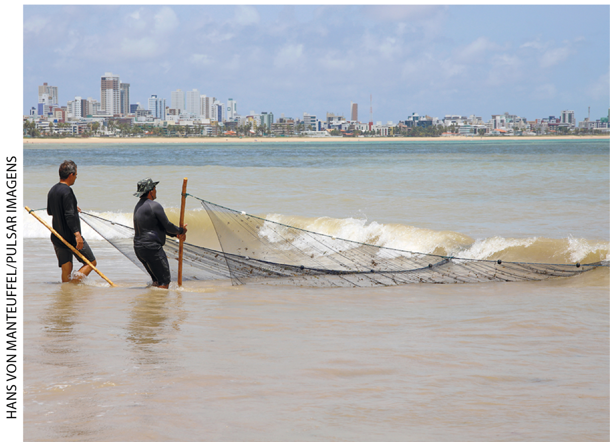 IMAGEM: d. dois pescadores recolhem uma rede na beira da praia. FIM DA IMAGEM.