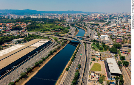 IMAGEM: vista aérea da cidade de são paulo cortada pelo rio tietê. avenidas largas e asfaltadas ladeiam o rio, que é cruzado por viadutos e pontes. FIM DA IMAGEM.