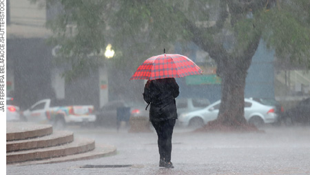 IMAGEM: um pedestre anda pela rua com um guarda-chuva aberto em um dia chuvoso. FIM DA IMAGEM.
