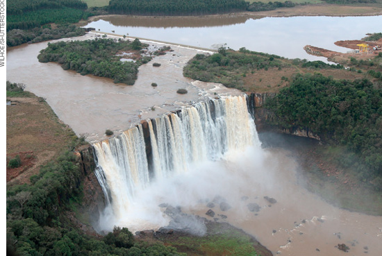 IMAGEM: fotografia aérea de uma região com um rio largo e um desnível brusco, formando uma cachoeira alta com grande volume de água. FIM DA IMAGEM.