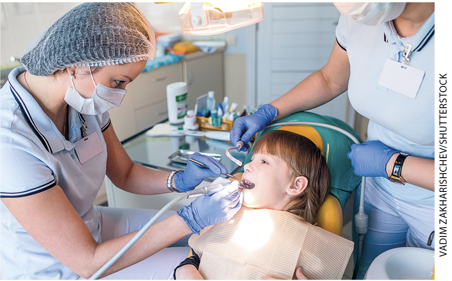 IMAGEM: 1. uma dentista cuida da boca de uma criança em um consultório. FIM DA IMAGEM.