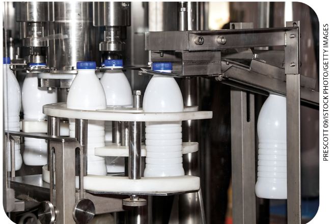 IMAGEM: 1. as garrafas de leite estão em máquinas, na indústria. FIM DA IMAGEM.