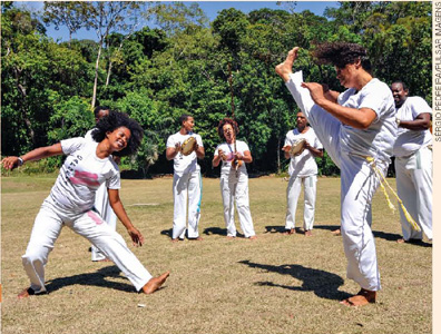 IMAGEM: grupo de capoeiristas praticando e tocando instrumentos típicos, como berimbau e pandeiro. FIM DA IMAGEM.