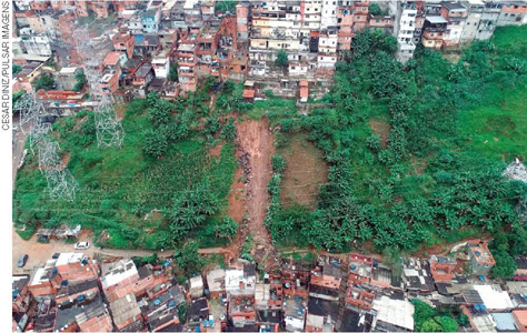 IMAGEM: vista aérea de um deslizamento de terra em um morro. acima e abaixo, grandes conjuntos de moradias em situação precária. FIM DA IMAGEM.