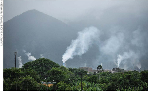 IMAGEM: montanhas em cubatão encobertas pela fumaça de chaminés industriais, cercadas por vegetação. FIM DA IMAGEM.