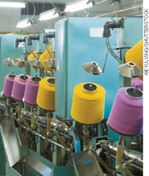 IMAGEM: uma máquina de costura industrial com bobinas de linha. FIM DA IMAGEM.