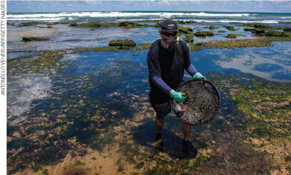 IMAGEM: um homem utiliza uma peneira para tirar óleo do oceano. FIM DA IMAGEM.