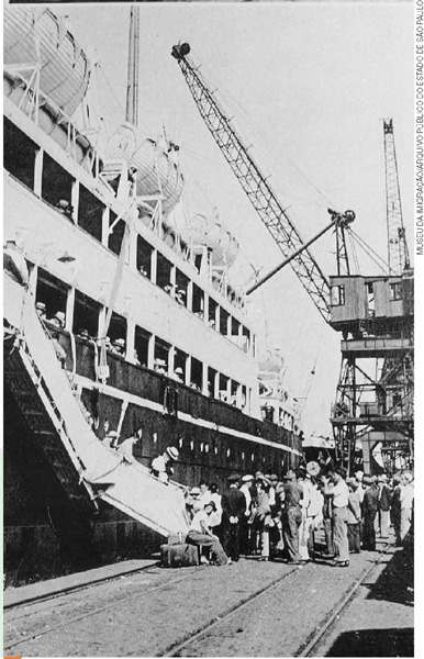 IMAGEM: foto histórica em preto e branco mostra imigrantes japoneses desembarcando de um grande navio. FIM DA IMAGEM.