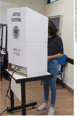 IMAGEM: uma mulher votando, seu rosto e sua identidade estão protegidos pela cabine de votação. FIM DA IMAGEM.