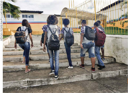 IMAGEM: um grupo de adolescentes uniformizados, com mochilas nas costas, sobem uma escada a caminho de uma escola. FIM DA IMAGEM.