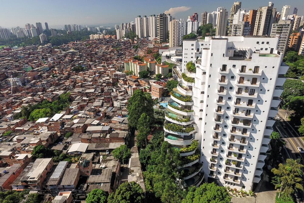 IMAGEM: vista aérea de área urbana com uma grande comunidade e um conjunto habitacional ao lado de prédios de luxo. FIM DA IMAGEM.