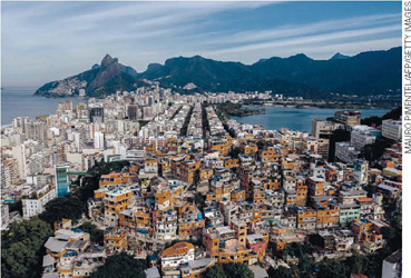 IMAGEM: uma fotografia aérea apresenta uma grande favela próxima a um complexo de prédios de luxo. próximo aos dois conjuntos residenciais, o mar, a baía de guanabara e o corcovado. FIM DA IMAGEM.