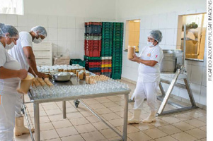IMAGEM: trabalhadores uniformizados produzem doces em uma fábrica. FIM DA IMAGEM.