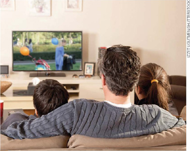 IMAGEM: uma família assiste televisão. FIM DA IMAGEM.