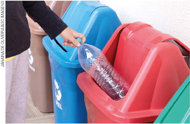 IMAGEM: uma pessoa descarta uma garrafa plástica na lixeira de material reciclável. FIM DA IMAGEM.
