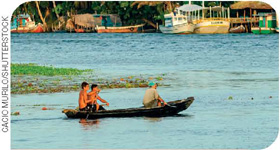IMAGEM: uma canoa pequena, navega perto da praia com três pessoas a bordo. FIM DA IMAGEM.