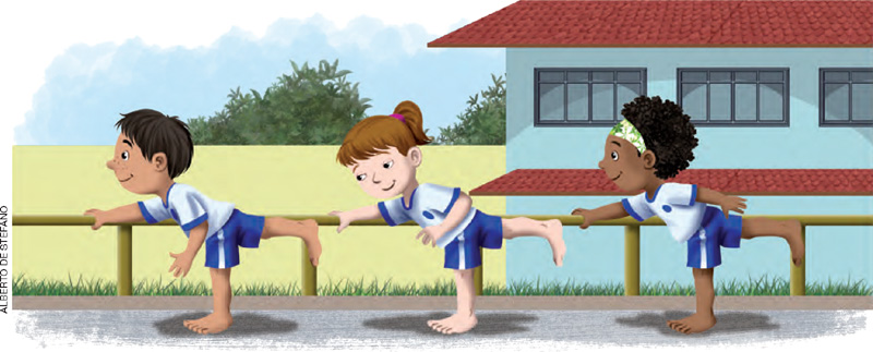 IMAGEM: três crianças alinhadas praticam movimentos de ginástica. elas se apoiam com as mãos em uma trave de madeira, com os corpos inclinados para a frente e uma perna flutuando no ar, enquanto se equilibram sobre a outra perna. ao fundo, uma construção grande e um campo com vegetação. FIM DA IMAGEM.